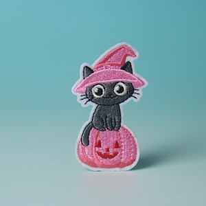 Peut inclure: Un chat noir portant un chapeau de sorcière rose est assis sur un potiron rose avec un visage de citrouille.