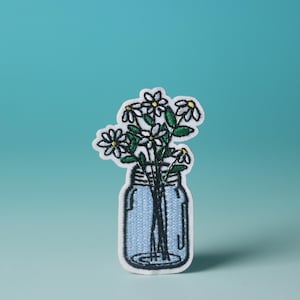 Könnte beinhalten: Weißer gestickter Aufnäher mit einem Einmachglas, gefüllt mit einem Strauß weißer Blumen mit grünen Stielen.