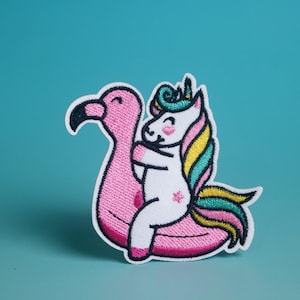 May include: Embroidered patch featuring a cartoon unicorn hugging a pink flamingo pool float. The unicorn has a white body, a colorful mane, and a star on its side. The patch has a white border and is set against a teal background.