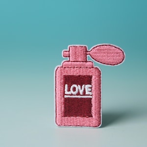 May include: Pink embroidered iron-on patch of a perfume bottle with the word "LOVE" in white lettering.