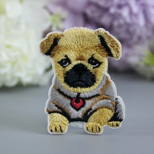 Puede incluir: Parche bordado para planchar de un pug marrón y beige que lleva un jersey gris con un corazón rojo en el cuello.