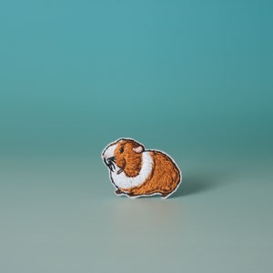 K&ouml;nnte beinhalten: Ein gestickter Aufn&auml;her mit einem braunen und wei&szlig;en Meerschweinchen. Das Meerschweinchen blickt nach links und hat einen wei&szlig;en Fleck um den Hals.