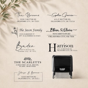 Op de afbeelding: Een zwarte zelfinktende Trodat-stempel naast acht verschillende adresstempelafdrukken. De afdrukken bevatten diverse namen en adressen, waaronder The Browns, Sophia Garcia, The Jason Family, Ethan and Olivia, Baden, Harrison, The Scarletts en Johnson and Brownes, weergegeven in verschillende lettertypes.