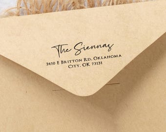 Może przedstawiać: Zbliżenie beżowej koperty z napisem "The Sienna's" elegancką czcionką. Poniżej adres: "2410 E Britton Rd, Oklahoma City, OK 73131" prostą czcionką. Koperta jest częściowo otwarta.