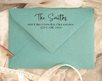 Może przedstawiać: Turkusowa koperta z napisem "The Smiths" elegancką czcionką. Poniżej adres: 2410 E Britton Rd, Oklahoma City, OK 73131. Widoczny dekoracyjny klucz i koronkowe wykończenie.