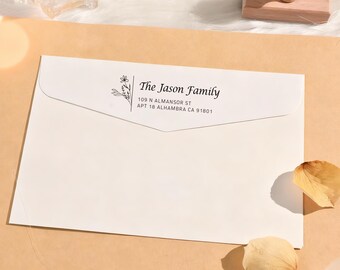 Może przedstawiać: Biała koperta z napisem "The Jason Family" i adresem w kolorze czarnym. Po lewej stronie tekstu znajduje się kwiatowa ilustracja. Koperta leży na jasnobrązowej powierzchni z suszonymi płatkami.