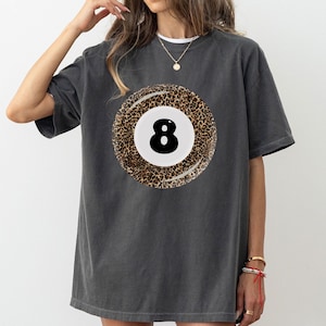 May include: A charcoal gray t-shirt with a graphic of a leopard print 8-ball.