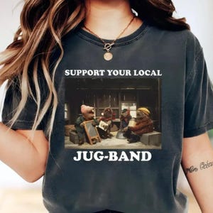 May include: Dark gray t-shirt with the text "SUPPORT YOUR LOCAL JUG-BAND." The graphic depicts a band of anthropomorphic creatures playing instruments. The image is in a vintage style.