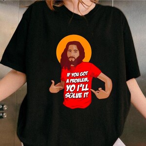 A person wearing a black t-shirt with a graphic design depicting a man with a beard and long hair, along with text that reads "If you got a problem, you'll solve it".