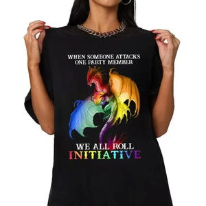 May include: Black t-shirt featuring a colorful dragon graphic with text. The dragon has red, orange, yellow, green, blue, and purple wings. The text reads "WHEN SOMEONE ATTACKS ONE PARTY MEMBER" and "WE ALL ROLL INITIATIVE".