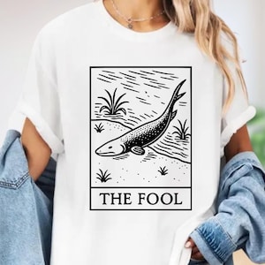 A white t-shirt with a graphic design depicting a fish and the text "THE FOL" printed on it.