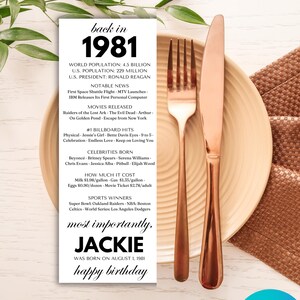 May include: A birthday-themed place setting with a rose gold fork and knife on a beige plate. A personalized card reads "back in 1981" with facts and the name "Jackie." The words "happy birthday" are also visible.