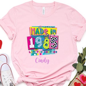 以下が含まれることがあります： ピンクのTシャツに、「Made in 1985 Limited Edition」というグラフィックデザインが施されています。ピンクのハートと「Cindy」という名前が下にあります。