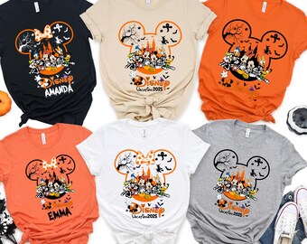 May include: A collection of short-sleeved t-shirts in various colors, featuring a Halloween-themed Disney design. The design includes Mickey Mouse ears, bats, and a group of Disney characters. Some shirts have names printed on them.
