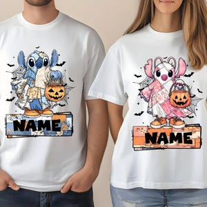 May include: White t-shirts with Halloween-themed cartoon characters. One shirt displays a blue character with a pumpkin bucket, the other a pink character with a jack-o'-lantern. Each shirt has a name banner.