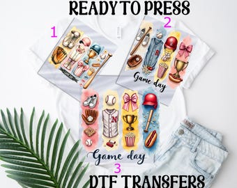 May include: White t-shirts with baseball-themed DTF transfers. The transfers feature baseball equipment, food, and text that says "Game Day". The text "READY TO PRESS" and "DTF TRANSFERS" are also visible.