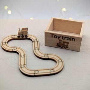 May include: A wooden toy train set with a track and a box. The track is a puzzle, and the train sits on top. The box is labeled "Toy train" with a train graphic.