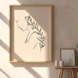 May include: A black and white line drawing of a person's face and shoulder with leaves growing from the shoulder. The drawing is on a beige background and is framed in a light wood frame.