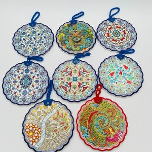 May include: Eight round ceramic wall hangings featuring intricate floral and geometric patterns in shades of blue, red, green, gold, and white. Each hanging has a blue cord loop for hanging.