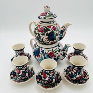 Könnte beinhalten: Ein Keramik-Teeservice mit Teekanne und Deckel sowie sechs Tassen und Untertassen. Das Set hat ein Blumenmuster in Rot, Blau und Grün auf cremefarbenem Grund. Die Teekanne ist etwa 20 cm hoch.