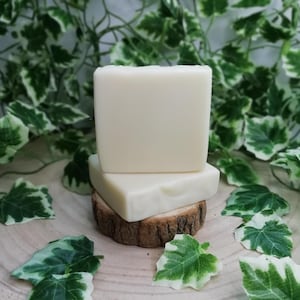 Puede incluir: Dos barras de jabón blancas apiladas una encima de la otra sobre una base de madera con hojas verdes esparcidas alrededor.