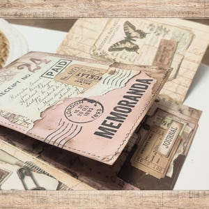 May include: A handmade paper journal featuring a collage of vintage-style ephemera, including a "MEMORANDA" stamp, a London postmark dated 1893, a "PAID" receipt, and a butterfly illustration. The cover has stitched edges and aged paper textures.