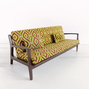 May include: A miniature brown wooden sofa with a green and brown patterned fabric upholstery and three matching cushions.