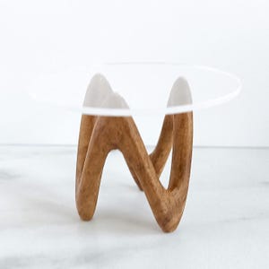 Peut inclure: Un petit présentoir composé d'un plateau circulaire en acrylique transparent reposant sur une base en bois clair. La base en bois présente une forme continue, angulaire et en zigzag qui assure la stabilité du plateau supérieur transparent.