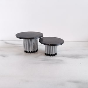 Op de afbeelding: Twee zwarte ronde tafelbladen met zilveren onderstellen. Het grotere tafelblad heeft een diameter van ongeveer 30 cm en het kleinere een diameter van ongeveer 20 cm.