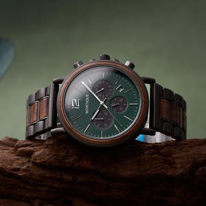 Puede incluir: Un elegante reloj de pulsera con esfera verde oscuro y bisel de madera. El reloj tiene una correa de metal negro con detalles de madera. La esfera muestra el n&uacute;mero 12 y la marca "Montique".