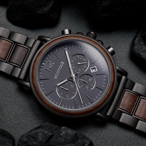May include: A wristwatch with a dark gray metal and brown wood link band. The round watch face is dark gray with silver hands, a date window, three sub-dials, and the word MONTIQUE printed in white. The bezel is framed in brown wood.
