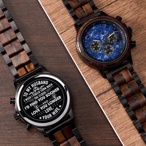 May include: Two wooden watches with black metal accents. One watch has a blue face with subdials, the other has a white face with text that reads "To my husband...I'd find you sooner...Love, your wife."