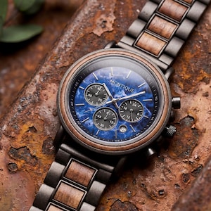Op de afbeelding: Een polshorloge met een blauwe marmeren wijzerplaat en houten accenten. Het horloge heeft een donkere metalen kast en band met houten schakels. De wijzerplaat heeft drie sub-wijzerplaten en de merknaam "MONTIQUE" is zichtbaar.