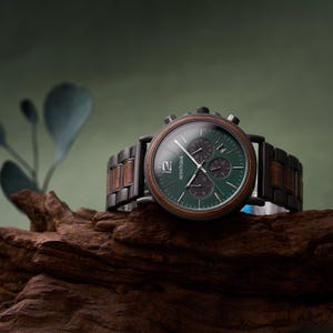 K&ouml;nnte beinhalten: Eine Armbanduhr mit dunkelgr&uuml;nem, rundem Zifferblatt, silbernen Zeigern und Datumsanzeige. Die Uhr hat eine h&ouml;lzerne L&uuml;nette und ein Armband aus dunklen Metallgliedern mit Holzakzenten. Das Wort MONTIQUE steht auf dem Zifferblatt neben der Ziffer 12.