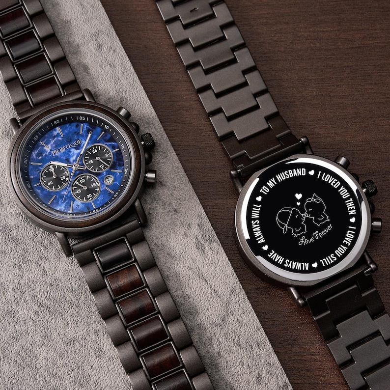 May include: Two dark wood and metal watches. One watch has a blue face with multiple dials and the word "PROFIQUE". The other watch has a black face with the words "TO MY HUSBAND, I LOVED YOU THEN, I LOVE YOU STILL, ALWAYS WILL, ALWAYS HAVE, Love Forever".