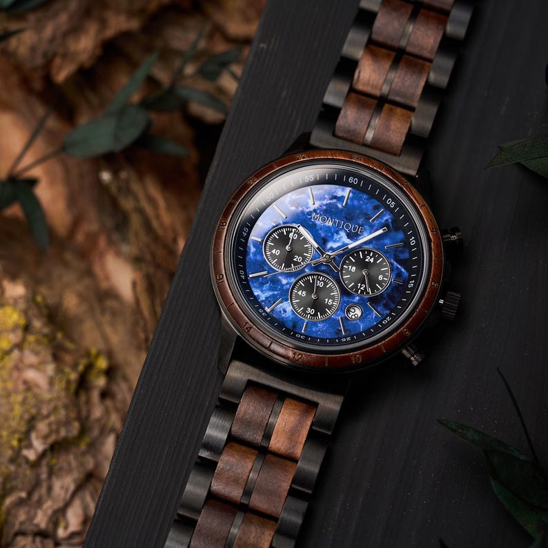 May include: A wristwatch with a wooden band and a blue face. The watch face has three sub-dials and the brand name "MONTIQUE". The watch has a dark brown wooden bezel and a dark metal case. The band is a combination of dark metal and wood.