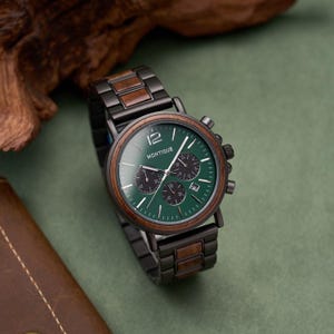 K&ouml;nnte beinhalten: Eine Armbanduhr mit einem Gliederarmband aus dunklem Metall und Holz, einem runden Geh&auml;use aus dunklem Metall mit Holzl&uuml;nette und einem gr&uuml;nen Zifferblatt mit dem Schriftzug MONTIQUE, drei Hilfszifferbl&auml;ttern, Datumsanzeige sowie silbernen Zeigern.