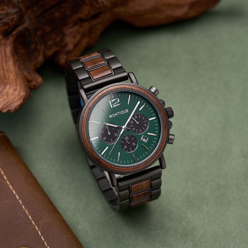 K&ouml;nnte beinhalten: Eine Armbanduhr mit einem Gliederarmband aus dunklem Metall und Holz, einem runden Geh&auml;use aus dunklem Metall mit Holzl&uuml;nette und einem gr&uuml;nen Zifferblatt mit dem Schriftzug MONTIQUE, drei Hilfszifferbl&auml;ttern, Datumsanzeige sowie silbernen Zeigern.