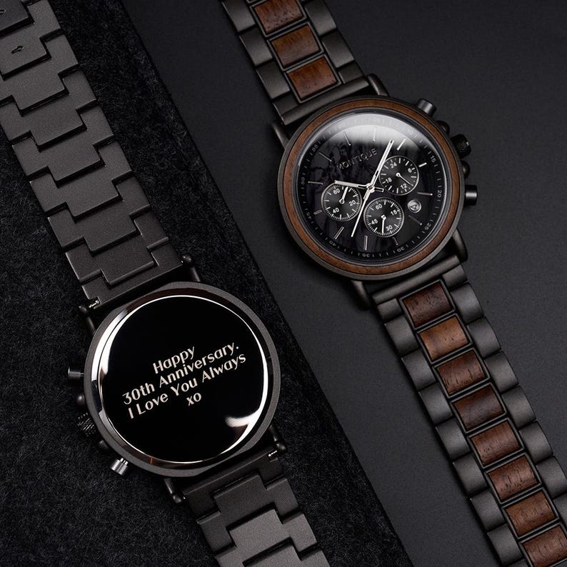 May include: Two black wooden watches with dark brown wood accents. One watch has a black face with multiple dials and the word "BOUTIQUE". The other watch has the message "Happy 30th Anniversary. I Love You Always xo" engraved on the face.