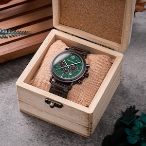 Puede incluir: Un reloj de madera con esfera verde y detalles negros, presentado en una caja de madera clara. El reloj lleva la marca "Montique" y muestra la fecha. La caja tiene un coj&iacute;n de tela de saco. La correa del reloj es marr&oacute;n oscuro.