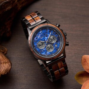 May include: A wristwatch with a blue marble-effect face and a wooden bezel and band. The watch face has multiple sub-dials and the brand name "MONTIQUE". The watch is set against a dark wood background.