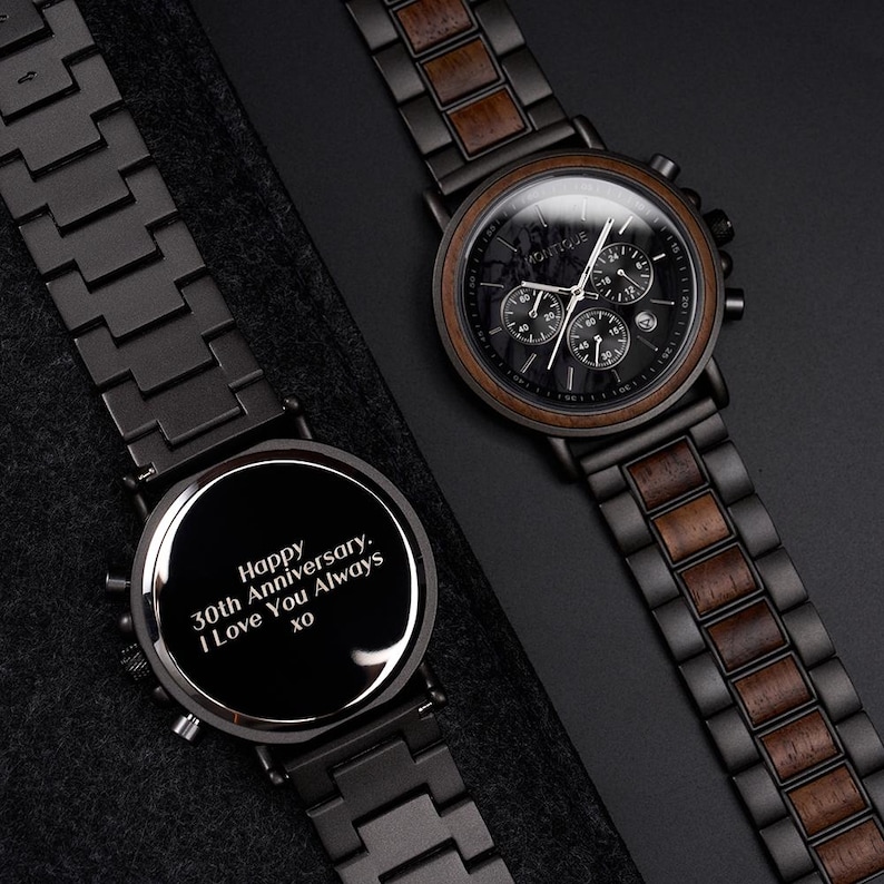 May include: Two black wooden watches with chronograph dials. One watch has a message engraved on the face that reads, "Happy 30th Anniversary. I Love You Always xo." The other watch has a wooden bezel and a black face with white hands.