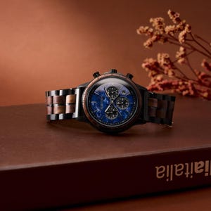 May include: A black and wood-toned wristwatch with a blue face and three sub-dials. The watch has a wooden band with alternating light and dark wood segments. The watch is displayed on a brown surface with a blurred background.