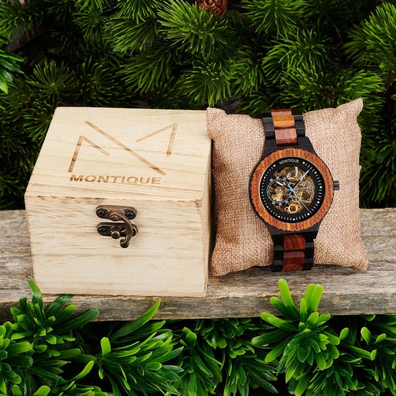 May include: A wooden watch with a black face and a brown and black wooden band. The watch has a skeleton movement and is packaged in a wooden box with the word "MONTIQUE" engraved on it.