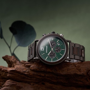 Puede incluir: Un reloj de pulsera de madera con esfera verde oscuro y correa de madera oscura. La esfera del reloj tiene tres subesferas y la marca "Montique" es visible. El reloj se muestra sobre un trozo de madera.