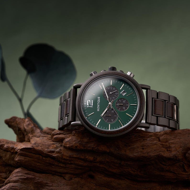 Puede incluir: Un reloj de pulsera de madera con esfera verde oscuro y correa de madera oscura. La esfera del reloj tiene tres subesferas y la marca "Montique" es visible. El reloj se muestra sobre un trozo de madera.