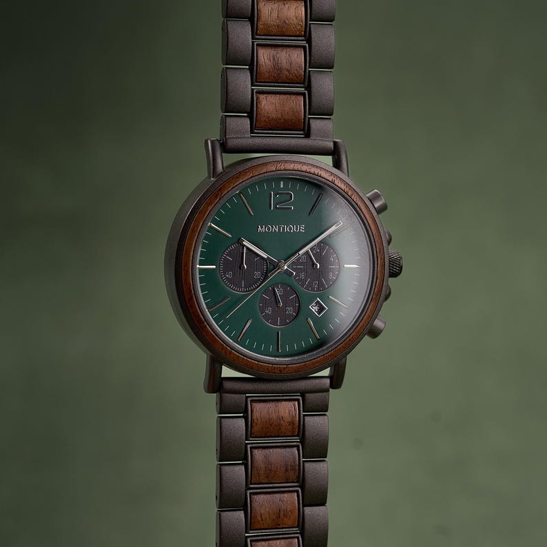 K&ouml;nnte beinhalten: Eine Armbanduhr mit dunkelgr&uuml;nem, rundem Zifferblatt, Holzl&uuml;nette und einem Gliederarmband aus abwechselnden dunklen Metall- und braunen Holzelementen. Das Zifferblatt zeigt den Markennamen Montique, drei Hilfszifferbl&auml;tter, ein Datumsfenster und silberne Zeiger.
