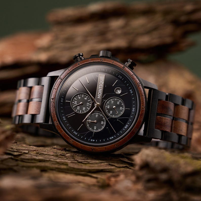Op de afbeelding: Een zwarte Montique chronograaf horloge met een houten rand en band. De wijzerplaat is zwart met drie sub-wijzerplaten en witte markeringen. De band is een combinatie van zwart metaal en houten schakels.
