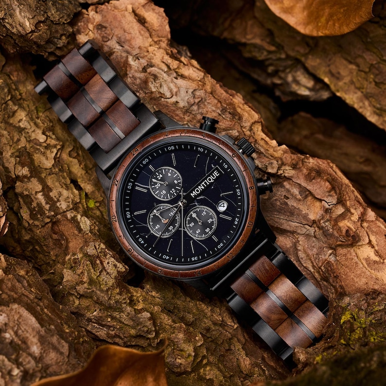 Op de afbeelding: Een Montique chronograaf horloge met een donkerblauwe wijzerplaat, meerdere sub-wijzerplaten en een datumvenster. Het horloge heeft een zwarte kast, een houten bezel en band. De band is gemaakt van afwisselend hout en zwarte metalen schakels.