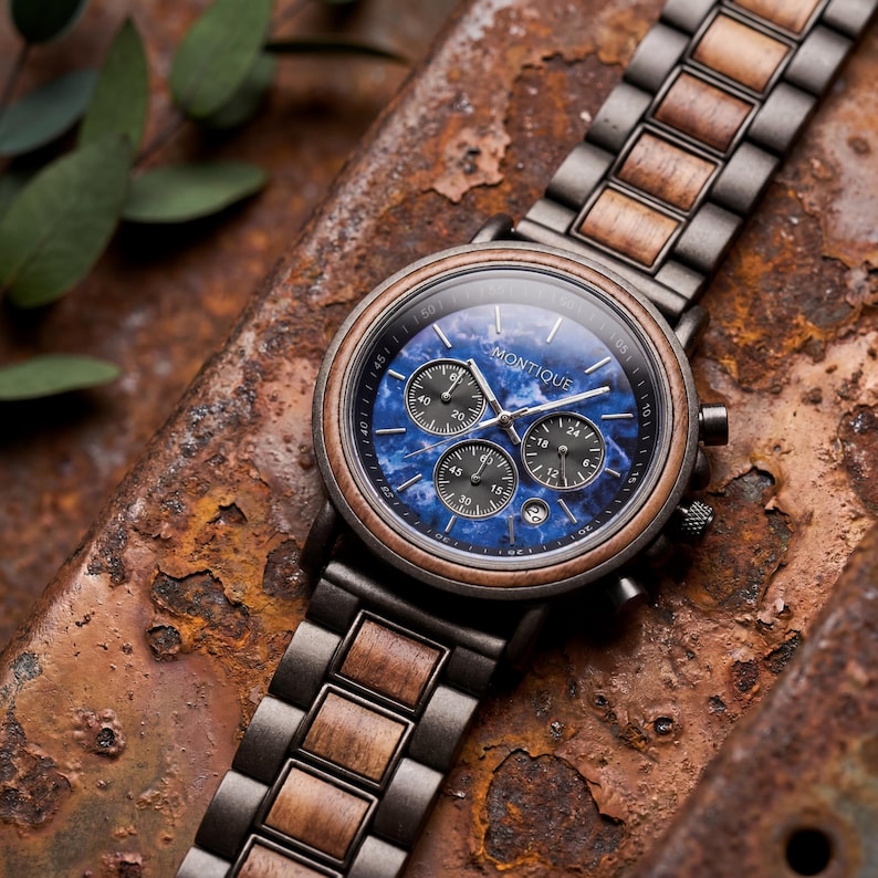 Op de afbeelding: Een polshorloge met een blauwe marmeren wijzerplaat en houten accenten. Het horloge heeft een donkere metalen kast en band met houten schakels. De wijzerplaat heeft drie sub-wijzerplaten en de merknaam "MONTIQUE" is zichtbaar.